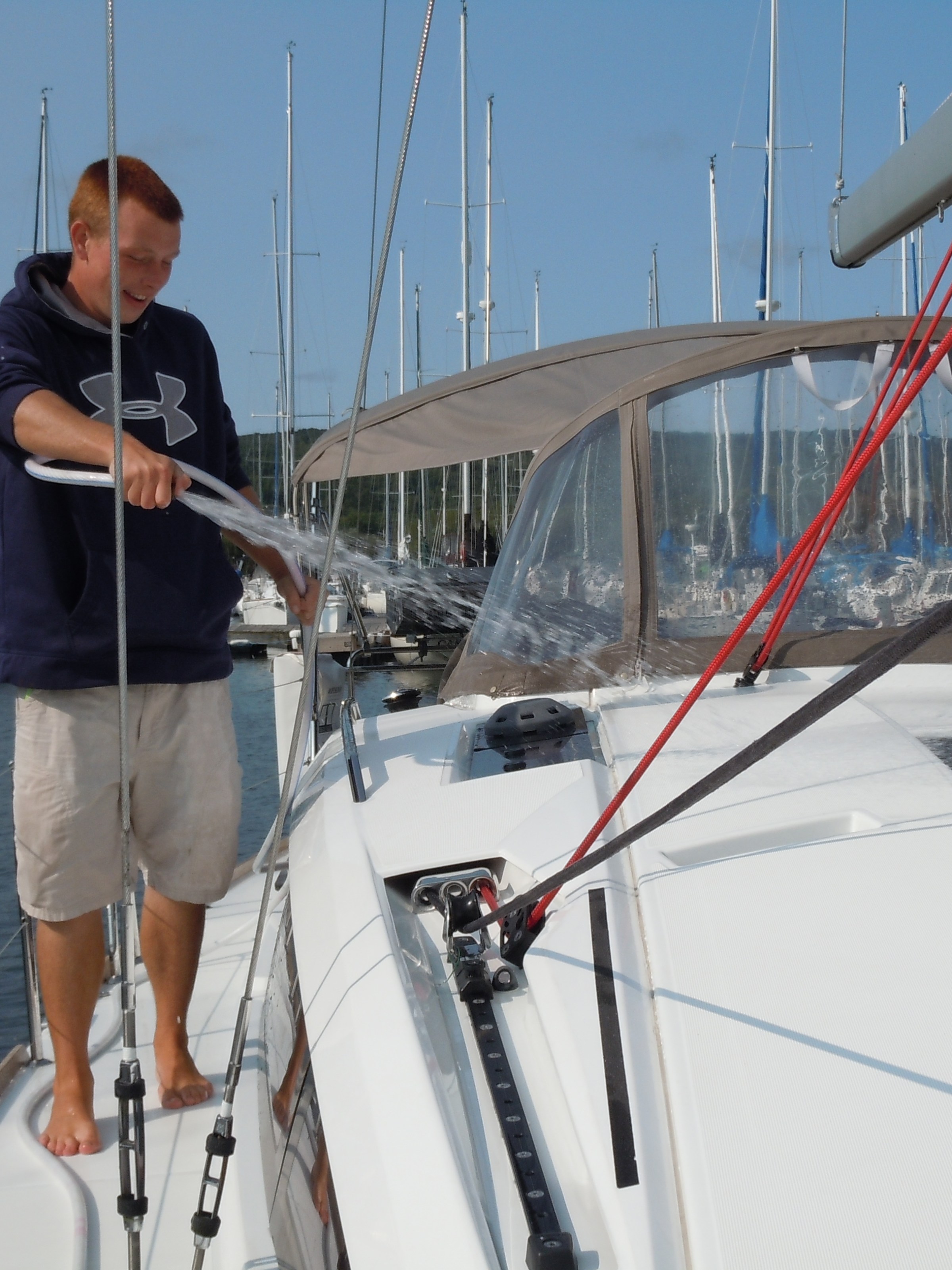 Crew member hosing off sailboat exterior