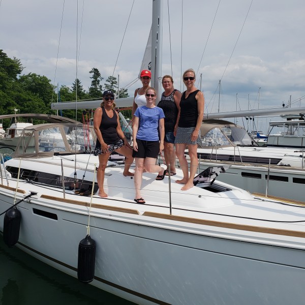 Group of girls standing on sailboat together at dock