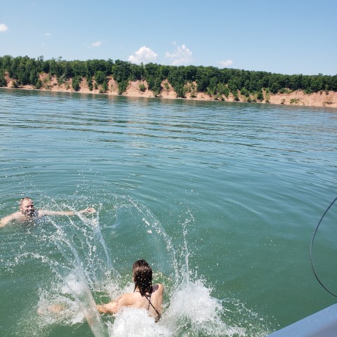 Two people jumping into blue lake from sailboat