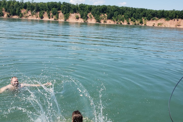 Two people jumping into blue lake from sailboat
