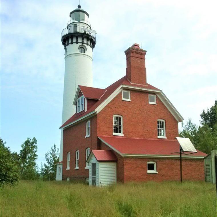 a lighthouse attached to a brick building on top of a lush green field