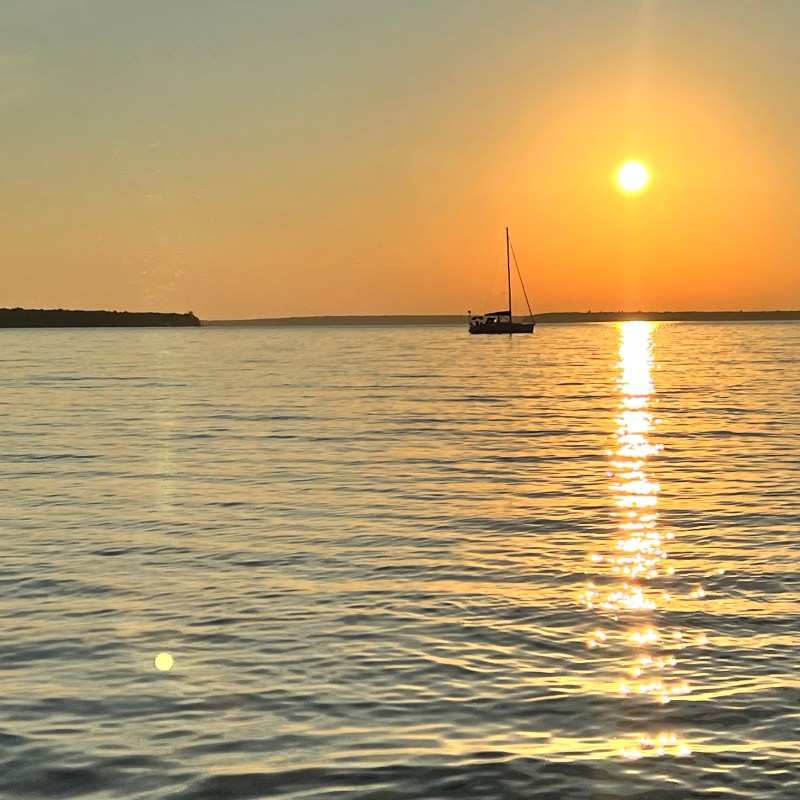 Sailboat on calm sea at sunset with sun reflection on water.