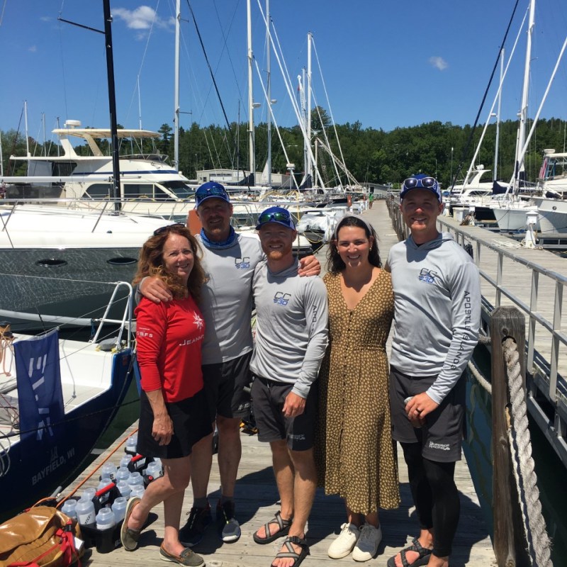 Group of people posing on a dock with sailboats in the background under a clear blue sky.