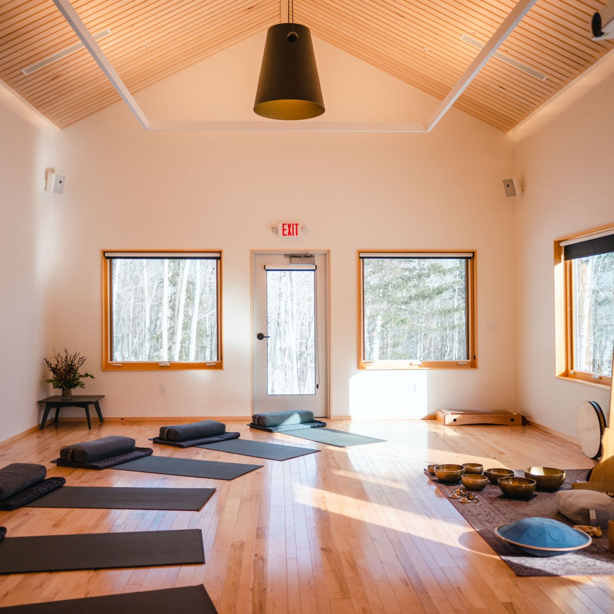 Spacious yoga studio with mats, cushions, and a large gong near a window.
