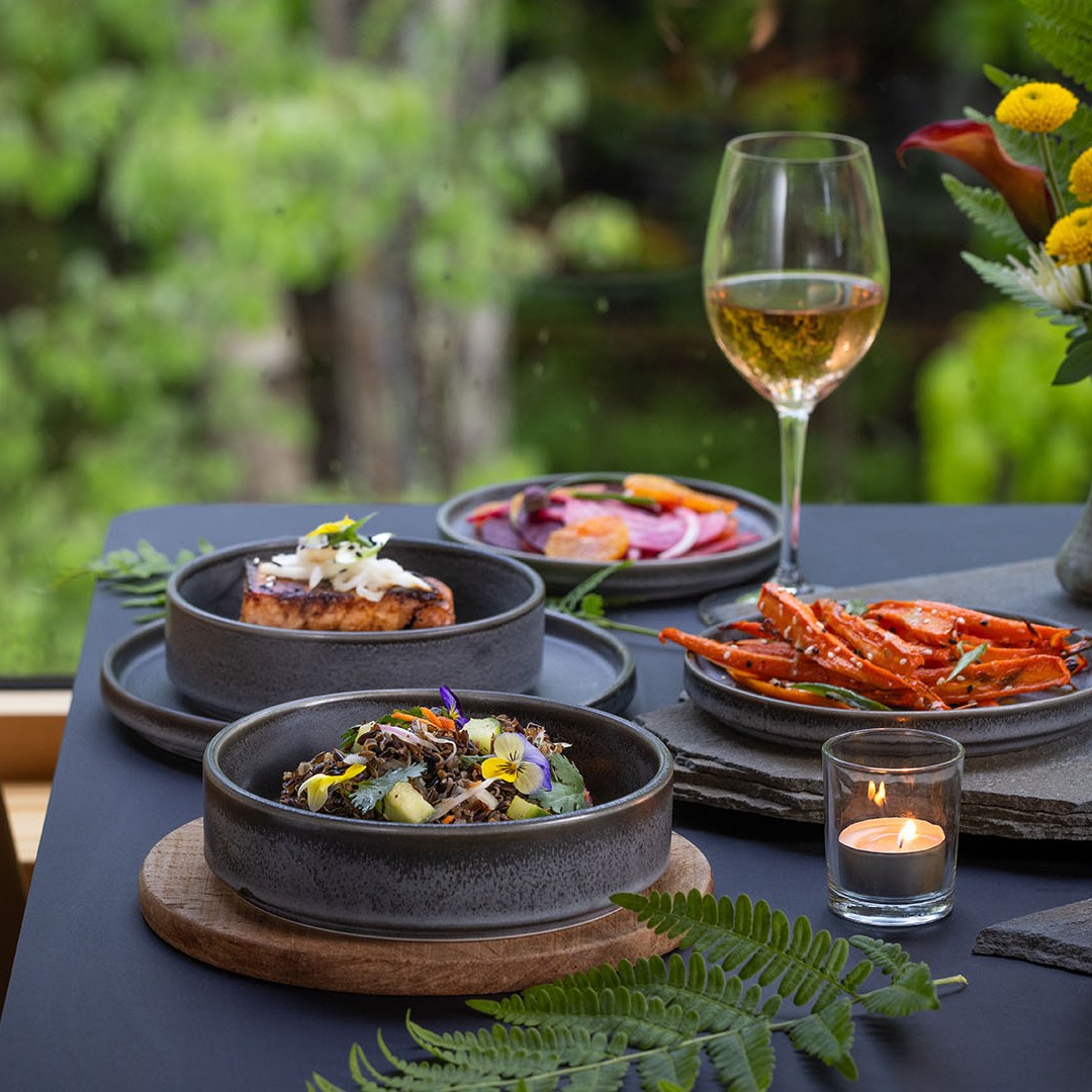 A table set with gourmet dishes, wine, candle, and flowers near a window.