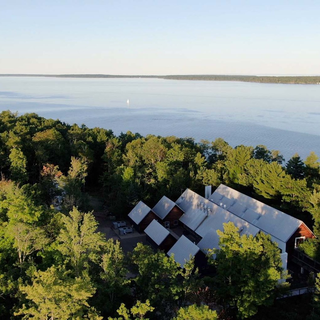 Aerial view of a large building surrounded by trees near a lakeshore.