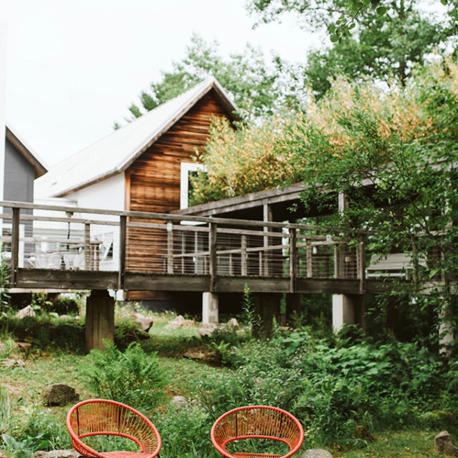 Two red chairs on grass with wooden house and trees in background.