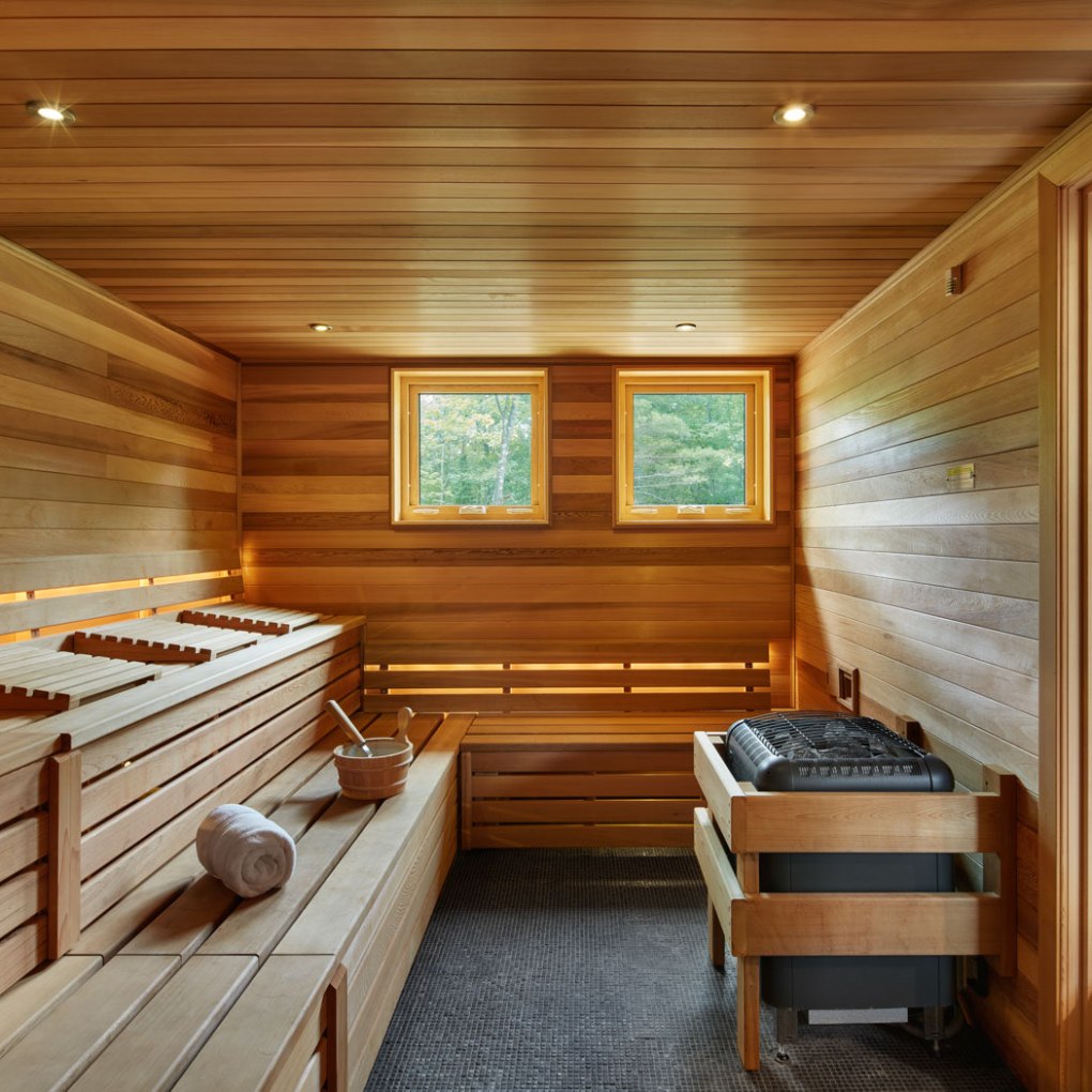 Wooden sauna room with benches, a heater, and two windows.